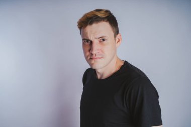 Stüdyoda poz ile genç bir adam. Kısa saç ve temiz cilt. Duygusal portre. Sokak tarzı giyim: siyah t-shirt ve kot pantolon