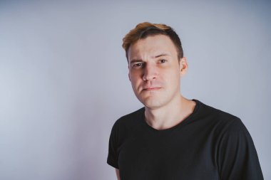 Stüdyoda poz ile genç bir adam. Kısa saç ve temiz cilt. Duygusal portre. Sokak tarzı giyim: siyah t-shirt ve kot pantolon