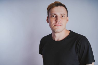 Stüdyoda poz ile genç bir adam. Kısa saç ve temiz cilt. Duygusal portre. Sokak tarzı giyim: siyah t-shirt ve kot pantolon