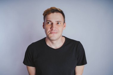 Stüdyoda poz ile genç bir adam. Kısa saç ve temiz cilt. Duygusal portre. Sokak tarzı giyim: siyah t-shirt ve kot pantolon