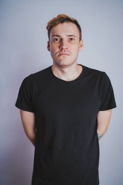 Stüdyoda poz ile genç bir adam. Kısa saç ve temiz cilt. Duygusal portre. Sokak tarzı giyim: siyah t-shirt ve kot pantolon