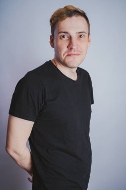 Stüdyoda poz ile genç bir adam. Kısa saç ve temiz cilt. Duygusal portre. Sokak tarzı giyim: siyah t-shirt ve kot pantolon