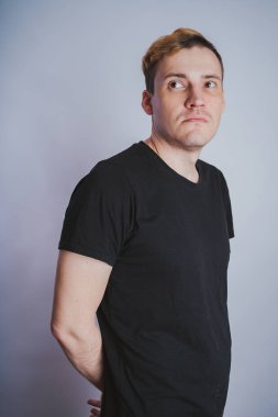 Stüdyoda poz ile genç bir adam. Kısa saç ve temiz cilt. Duygusal portre. Sokak tarzı giyim: siyah t-shirt ve kot pantolon