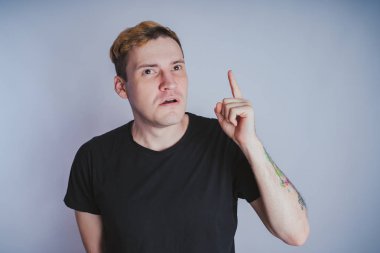 Stüdyoda poz ile genç bir adam. Kısa saç ve temiz cilt. Duygusal portre. Sokak tarzı giyim: siyah t-shirt ve kot pantolon