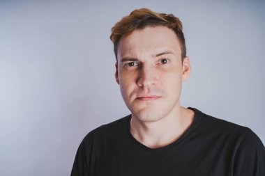 Stüdyoda poz ile genç bir adam. Kısa saç ve temiz cilt. Duygusal portre. Sokak tarzı giyim: siyah t-shirt ve kot pantolon