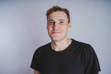 Stüdyoda poz ile genç bir adam. Kısa saç ve temiz cilt. Duygusal portre. Sokak tarzı giyim: siyah t-shirt ve kot pantolon