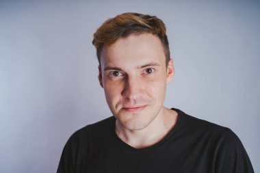 Stüdyoda poz ile genç bir adam. Kısa saç ve temiz cilt. Duygusal portre. Sokak tarzı giyim: siyah t-shirt ve kot pantolon