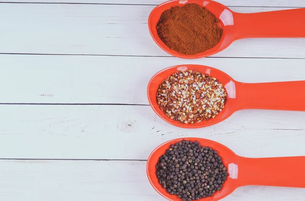 stock image Spices in orange spoon on white wooden background. seasoning delicious food. Paprika, black pepper peas, Gross natural sea salt mixed with dried red hot chili pepper, colorful seasoning close-up