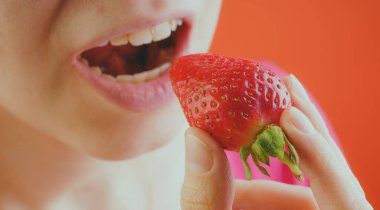 Taze çilek yiyen bir kadın, yakın plan. Bir kadının elinde kırmızı çilek. Meyve, sağlıklı bir diyetin ve ince bir vücudun anahtarıdır..