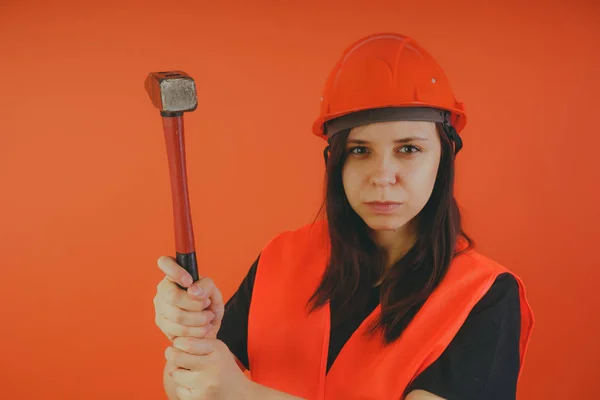 Girl Builder with hammer in hand, concept: girl doing repairs. A woman in a helmet and an orange vest, in the image of a road worker or surveyor