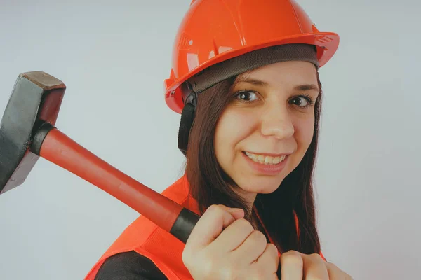 Girl Builder with hammer in hand, concept: girl doing repairs. A woman in a helmet and an orange vest, in the image of a road worker or surveyor