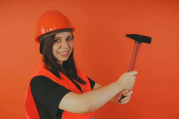 Girl Builder with hammer in hand, concept: girl doing repairs. A woman in a helmet and an orange vest, in the image of a road worker or surveyor