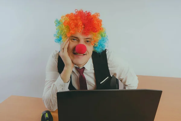 Office worker in clown wig, clown concept at work. Businessman at the computer, work on a laptop