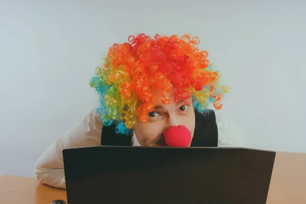 Office worker in clown wig, clown concept at work. Businessman at the computer, work on a laptop