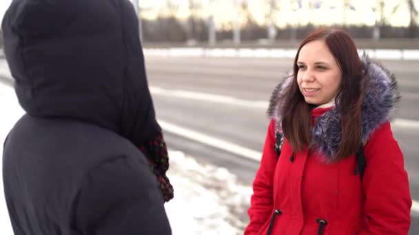 Dos hermosas mujeres paseando por la calle en invierno y charlando bien. Mujeres vestidas de colores cálidos que caminan con un clima frío. — Vídeos de Stock