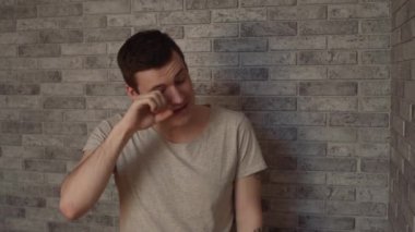 Genç, uykulu bir adam tuğla bir arka planda.