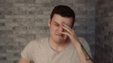 Genç, uykulu bir adam tuğla bir arka planda.