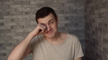 Genç, uykulu bir adam tuğla bir arka planda.