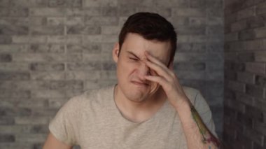 Genç, uykulu bir adam tuğla bir arka planda.