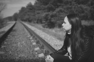 Düşünceli kadın demiryolunda oturuyor. Siyah beyaz, düşünceli genç bir kadın, demiryolunda oturuyor ve doğaya bakıyor.