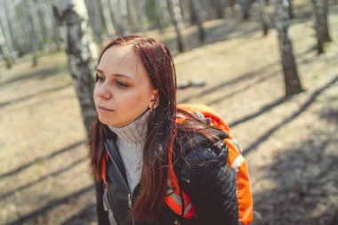 Ormanda sırt çantası ile seyahat eden kadın sakin güneşli ormanda parlak turuncu sırt çantası ile duran esmer Yan görünümü uzağa bakan