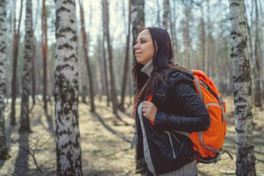 Ormanda sırt çantası ile seyahat eden kadın sakin güneşli ormanda parlak turuncu sırt çantası ile duran esmer Yan görünümü uzağa bakan