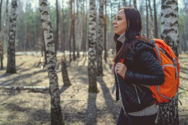 Kadın esmer duran woodsside görünümünde sırt çantası ile parlak turuncu sırt çantası uzağa bakarak sakin güneşli orman ile seyahat