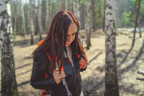 Traveling woman with backpack in woods Side view of brunette standing with bright orange backpack in tranquil sunny forest looking away