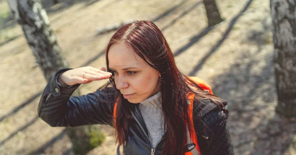 Traveling woman with backpack in woods Side view of brunette standing with bright orange backpack in tranquil sunny forest looking away