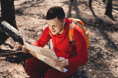 Adam woodsyoung dostum ormandaki düşmüş ağaç gövdesi üzerinde oturan ve sırt çantası ile seyahat ederken haritaya kırmızı spor içinde ilham harita okuma sırt çantası ile