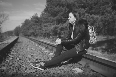 Düşünceli kadın demiryolunda oturuyor. Siyah beyaz, düşünceli genç bir kadın, demiryolunda oturuyor ve doğaya bakıyor.