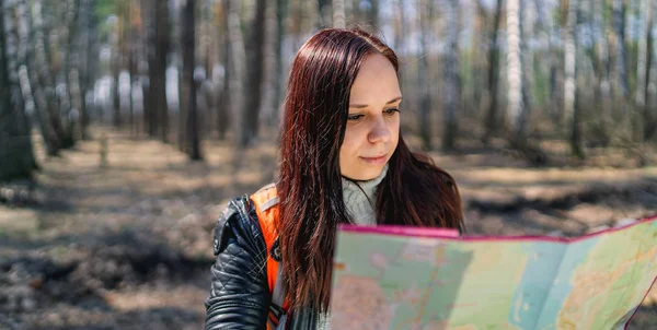 Traveling woman with map in woods From below of woman with backpack sitting on log in woods reading map in sunlight