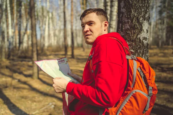 Traveling man with map in woods.Side view of man with backpack reading map looking away among trees in sunny forest. A man lost in the woods