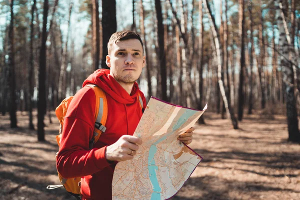 Traveling man with map in woods.Side view of man with backpack reading map looking away among trees in sunny forest. A man lost in the woods