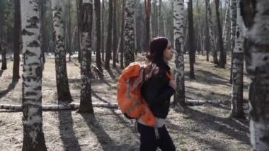 Ormanda sırt çantası ile seyahat eden kadın sakin güneşli ormanda parlak turuncu sırt çantası ile duran esmer Yan görünümü uzağa bakan