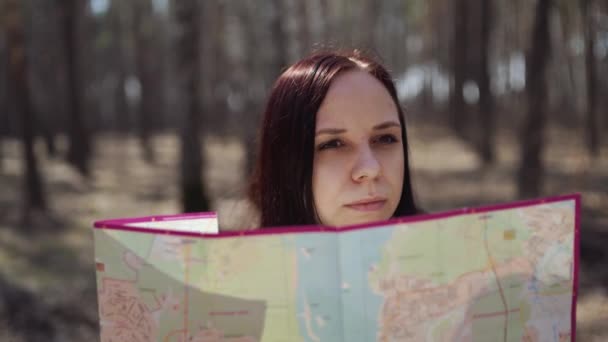 森の中で地図を持つ旅の女性 日差しの中で地図を読む 森の中の丸太に座っているバックパックを持つ女性の下から — ストック動画