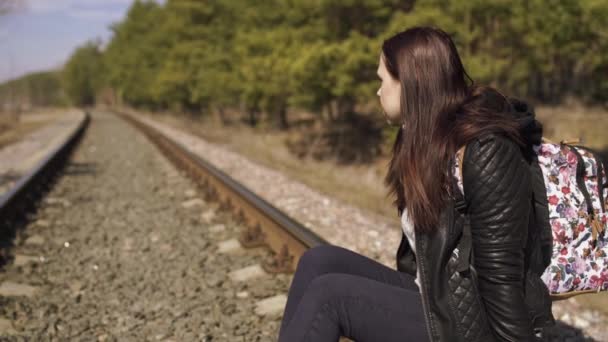 鉄道に座っているペンシブな女性 レールの上に座って自然の中を見つめている若い思慮深い女性の側面図 — ストック動画