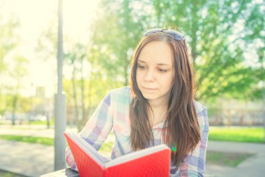 Parkta elinde kitap olan bir kadın. Bayan, öğrenci parkta bankta oturan ilginç bir kitap okuyor.