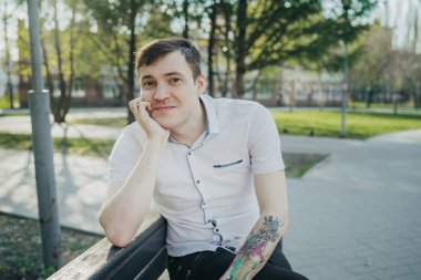 Parkta kolunda dövme olan bir adam. Yakışıklı bir adam parkta bir bankta dinleniyor..