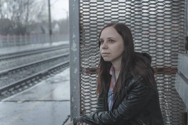 在阴云密布的日子里 一个穿着皮夹克坐在铁路的年轻女子坐在铁道旁边的梦幻的年轻女子的侧影 — 图库照片