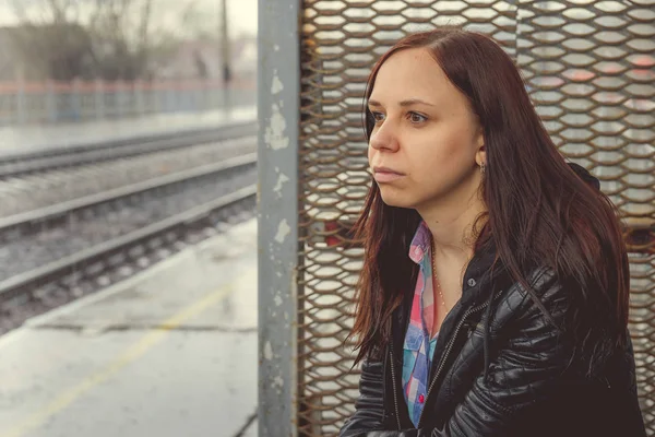 在阴云密布的日子里 一个穿着皮夹克坐在铁路的年轻女子坐在铁道旁边的梦幻的年轻女子的侧影 — 图库照片