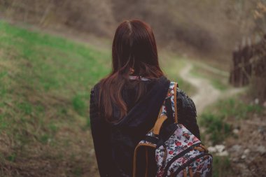 Yürüyen genç bir kadın. Renkli sırt çantalı genç bir bayanın bahar günü kırsala inişi.