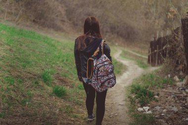 Yürüyen genç bir kadın. Renkli sırt çantalı genç bir bayanın bahar günü kırsala inişi.