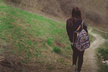 Yürüyen genç bir kadın. Renkli sırt çantalı genç bir bayanın bahar günü kırsala inişi.