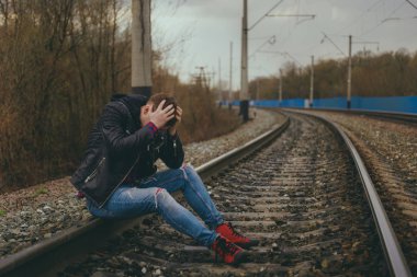 Demiryolunda oturan umutsuz adam. Sonbahar kırsalında raylarda otururken kafasına dokunan sıradan giysili umutsuz bir erkeğin yan görüntüsü