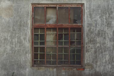 Eski ahşap pencere çerçevesinde kırık camlar ve eski terk edilmiş tuğla binada kısmen kırılmış camlar.