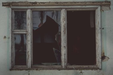 Eski ahşap pencere çerçevesinde kırık camlar ve eski terk edilmiş tuğla binada kısmen kırılmış camlar.