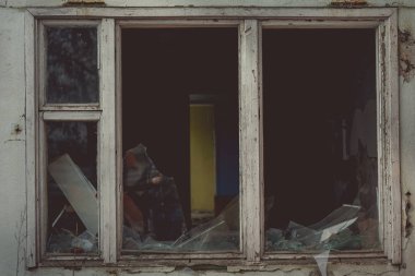 Eski ahşap pencere çerçevesinde kırık camlar ve eski terk edilmiş tuğla binada kısmen kırılmış camlar.