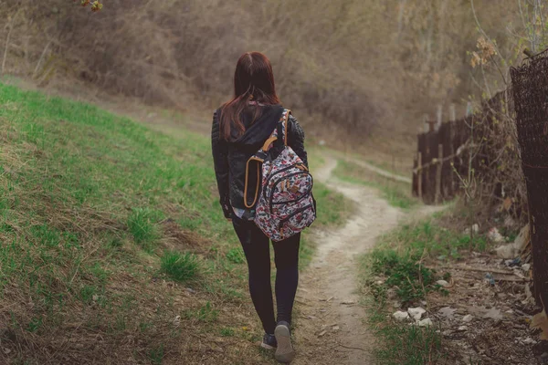 Yürüyen genç bir kadın. Renkli sırt çantalı genç bir bayanın bahar günü kırsala inişi.