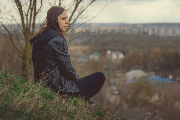 Yeşil tepede oturan genç bir kadın. Yükseklerde oturan ve bahar günü banliyöye bakan rüya gibi genç bir kadının yan görüntüsü.